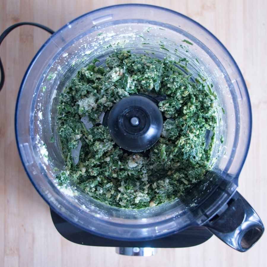 Blending fresh garlic leaves, walnuts, and cheese in a food processor to form a coarse green paste