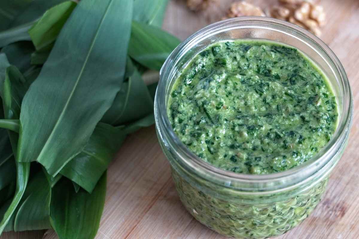 Jar of wild garlic pesto with a coarse texture, placed on a wooden board with fresh wild garlic leaves beside it