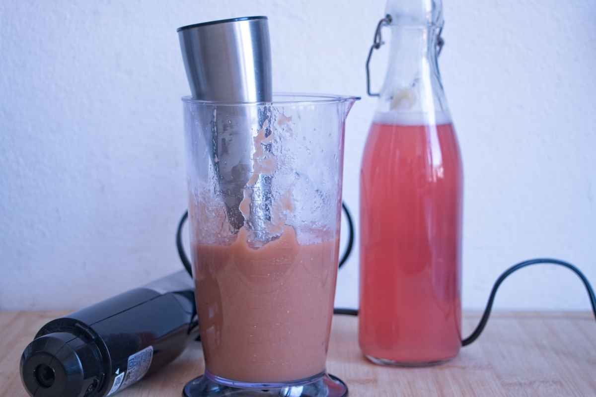 Blended rhubarb pulp in a jug with stick blender next to bottle of cordial