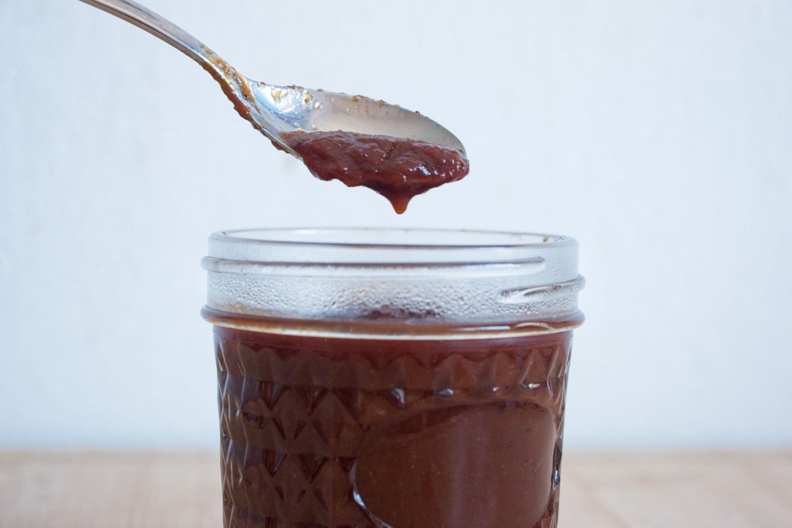 Homemade brown sauce recipe dripping from a spoon into a jar, showing thick, glossy texture