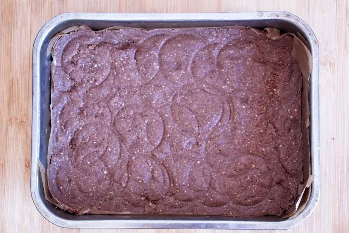 Protein bar mixture pressed firmly into a lined baking tin before chilling