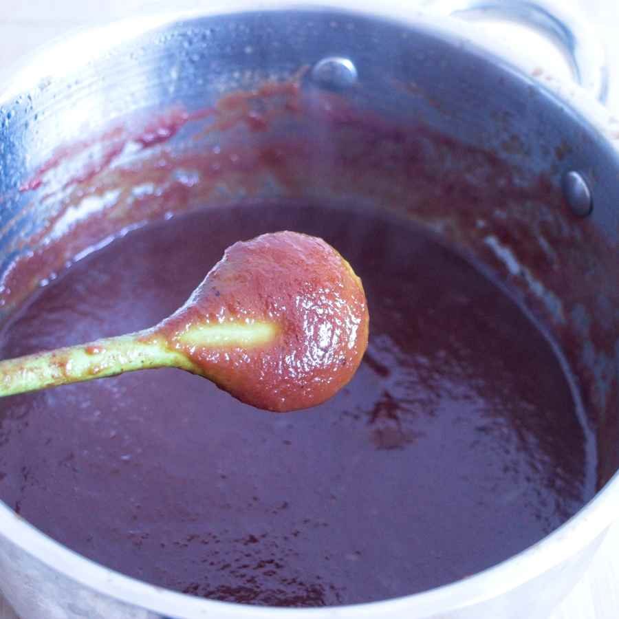 Reducing brown sauce in a saucepan, showing thickening texture on a spoon