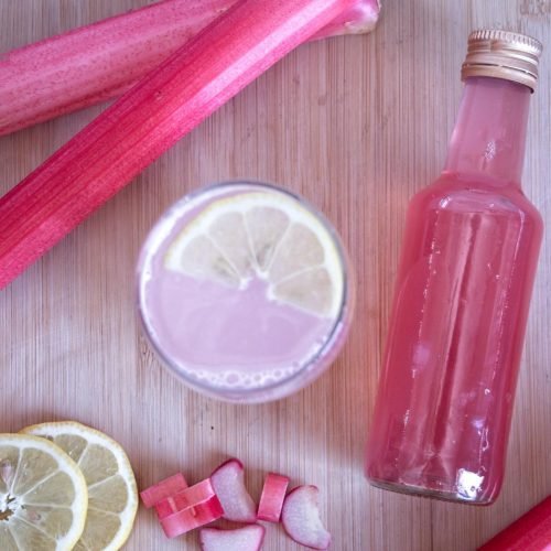 Overhead view of rhubarb ginger cordial with lemon slices, fresh rhubarb, and bottle of rhubarb ginger cordial