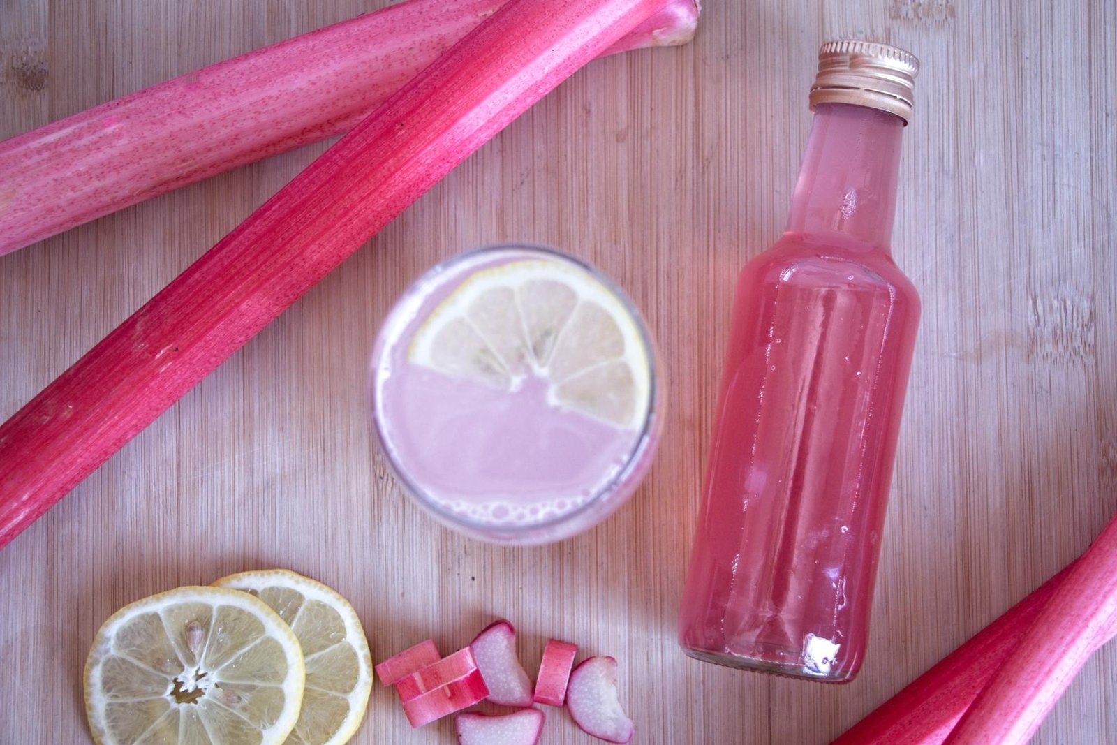 Overhead view of rhubarb ginger cordial with lemon slices, fresh rhubarb, and bottle of rhubarb ginger cordial