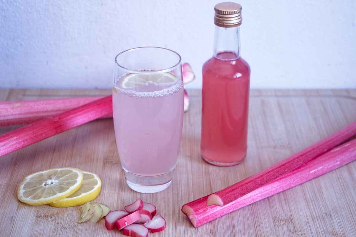 Glass of rhubarb ginger cordial with lemon and bottle of homemade rhubarb ginger cordial on wooden surface