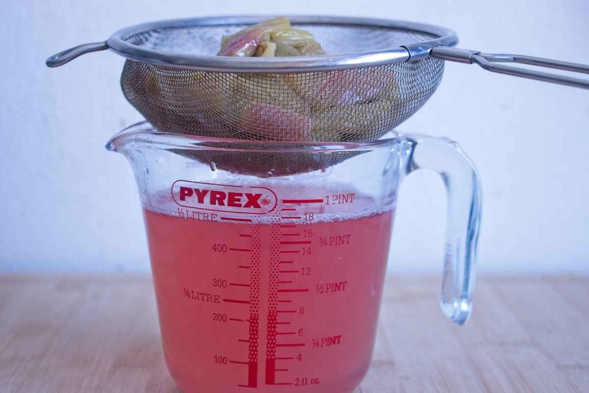 Straining cooked rhubarb through a sieve into a jug to make cordial