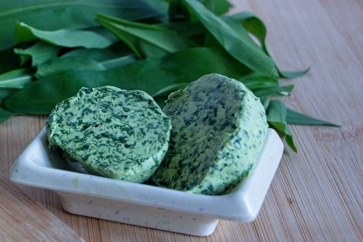 Sliced wild garlic butter rounds in a small dish with fresh leaves in the background