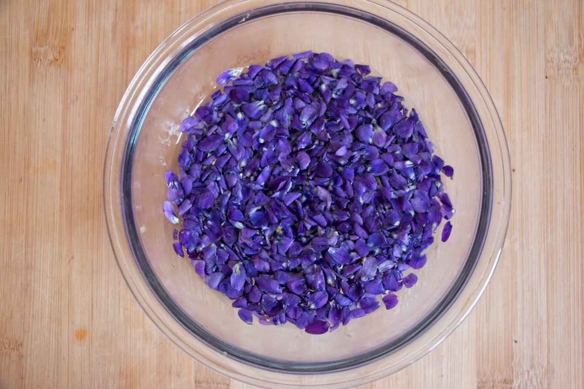 Bowl of fresh violet petals ready for infusing on a wooden surface