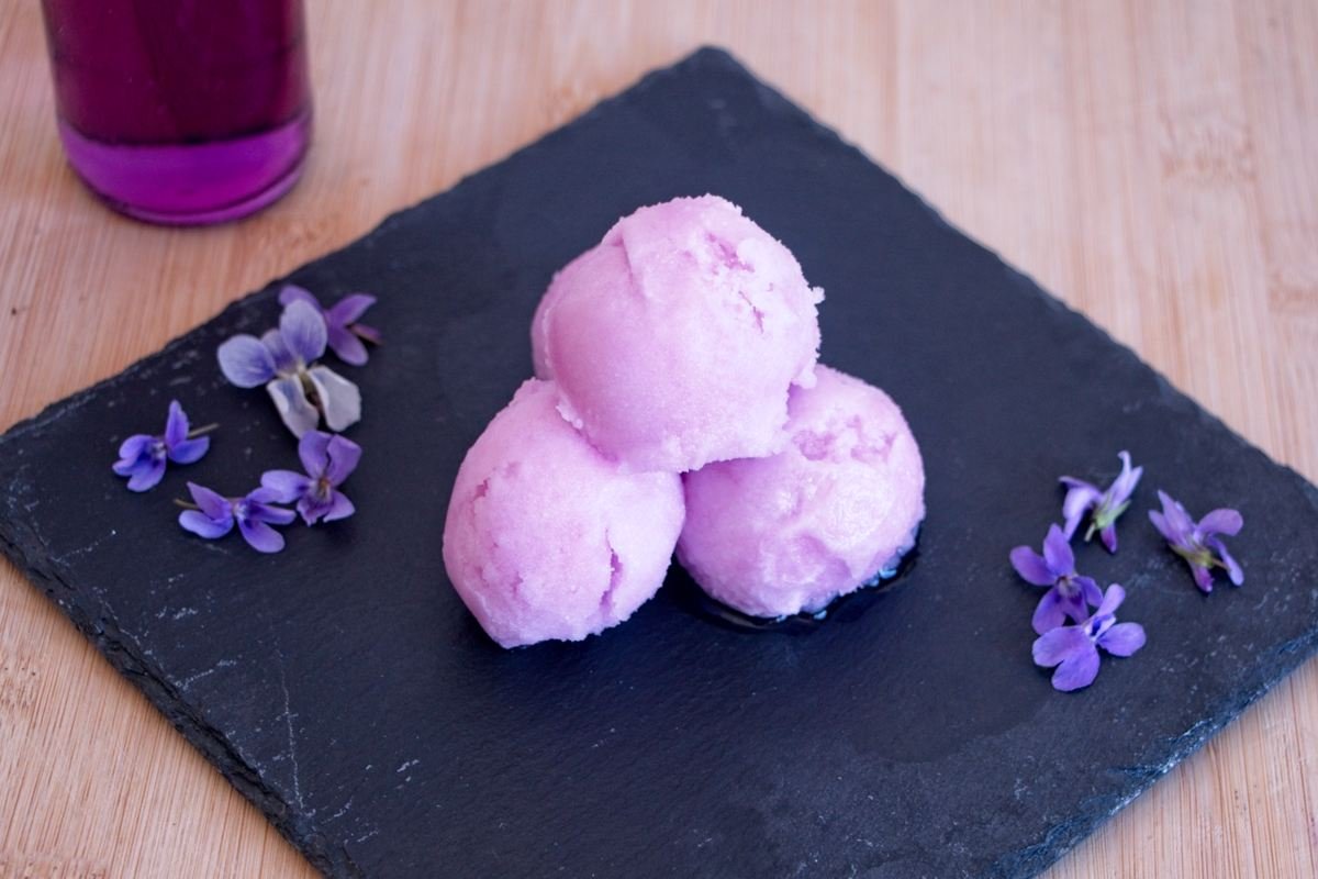 three scoops of violet sorbet served on black slate with fresh violet flowers
