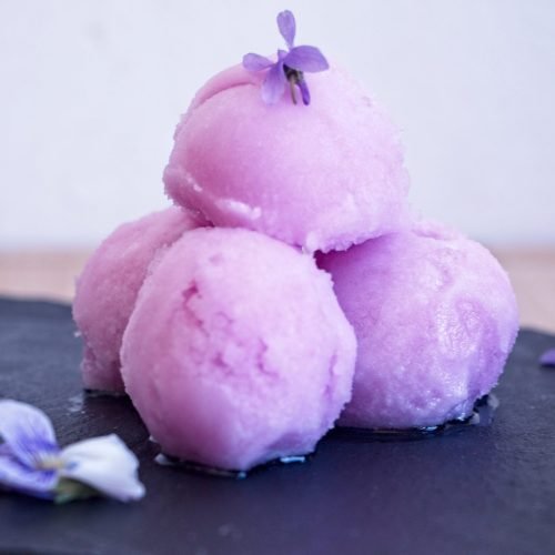 violet sorbet recipe hero image with scoops on black slate and fresh violet flowers