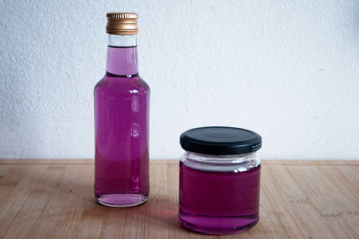 Bottle and jar of violet syrup on a wooden surface showing rich purple colour