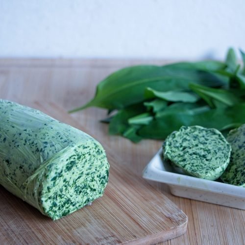 Sliced wild garlic butter with a rolled log and fresh leaves on a wooden board