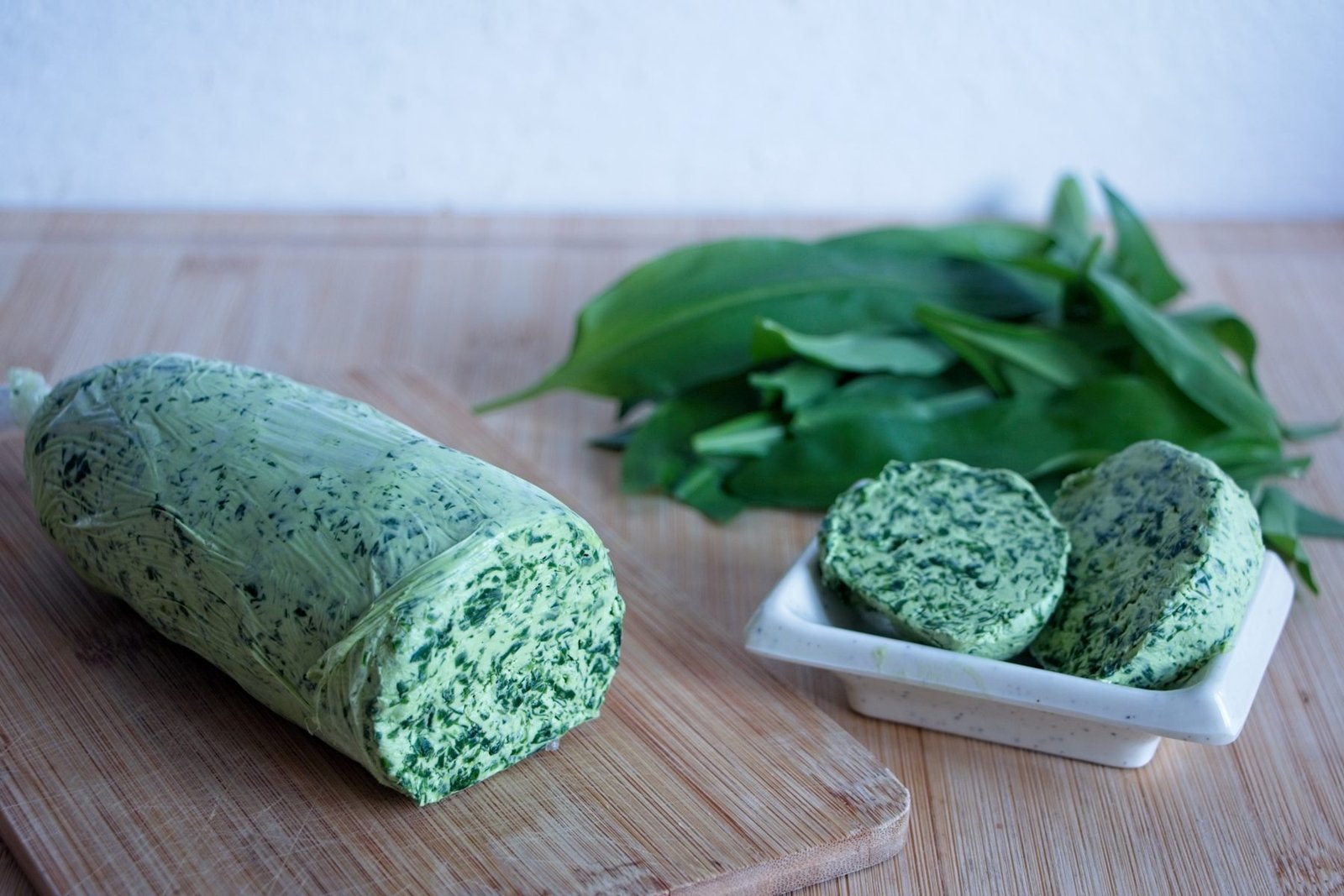 Sliced wild garlic butter with a rolled log and fresh leaves on a wooden board