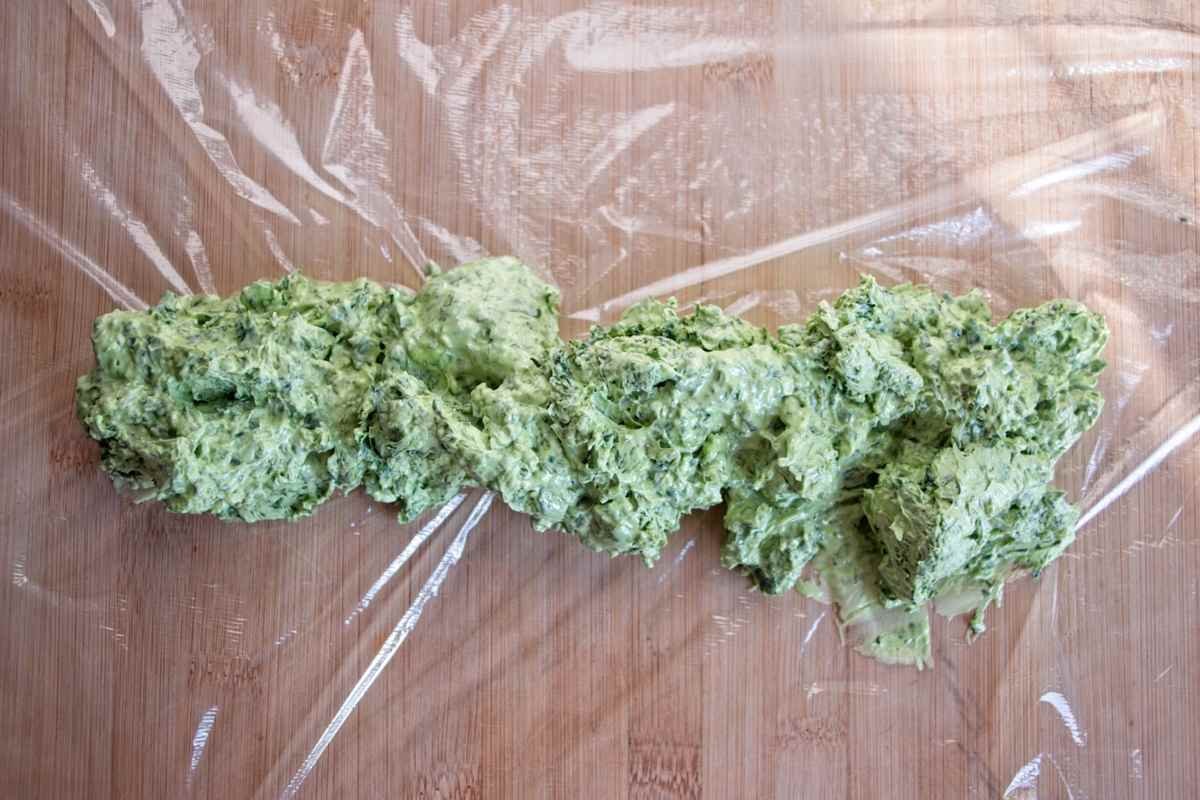 Green garlic butter mixture being shaped into a log on cling film
