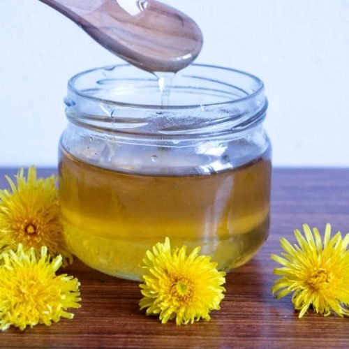 dandelion honey dripping from spoon into glass jar