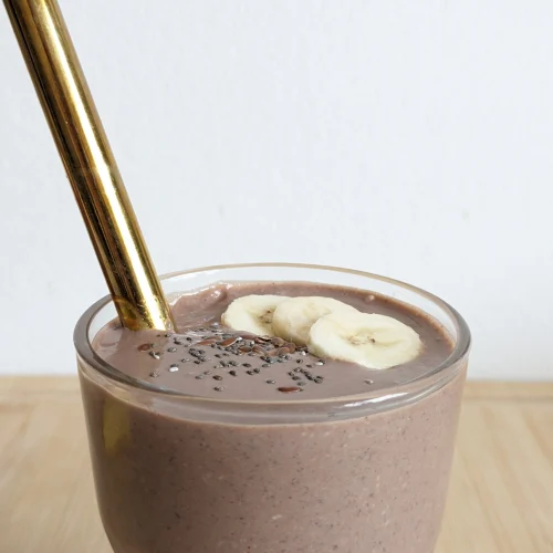 Chocolate high protein breakfast smoothie with a reusable metal straw, topped with banana slices, chia seeds and ground flaxseed.