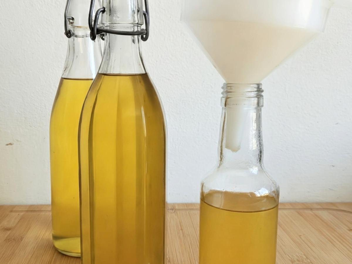 Homemade Mirabelle plum cordial being poured through a funnel into glass bottles.