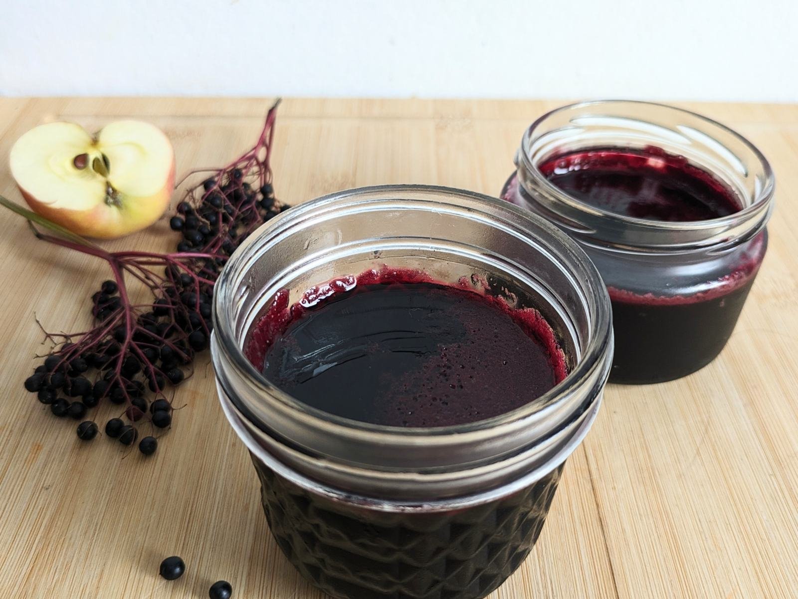 Homemade elderberry jelly in jars with fresh elderberries and apple
