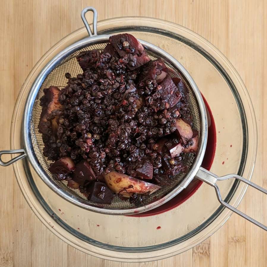 Cooked elderberries and apple being pressed through a sieve