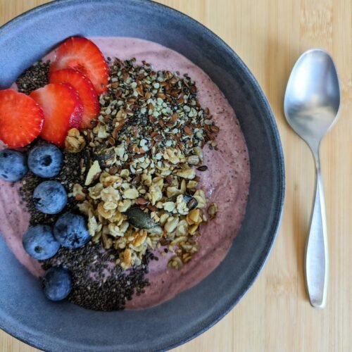 High fibre berry smoothie bowl topped with fresh berries, chia seeds, granola and mixed seeds.