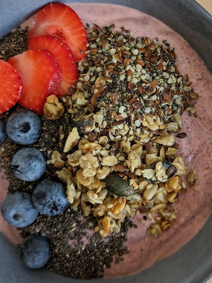 High fibre berry smoothie bowl topped with strawberries, blueberries, chia seeds, mixed seeds and granola.