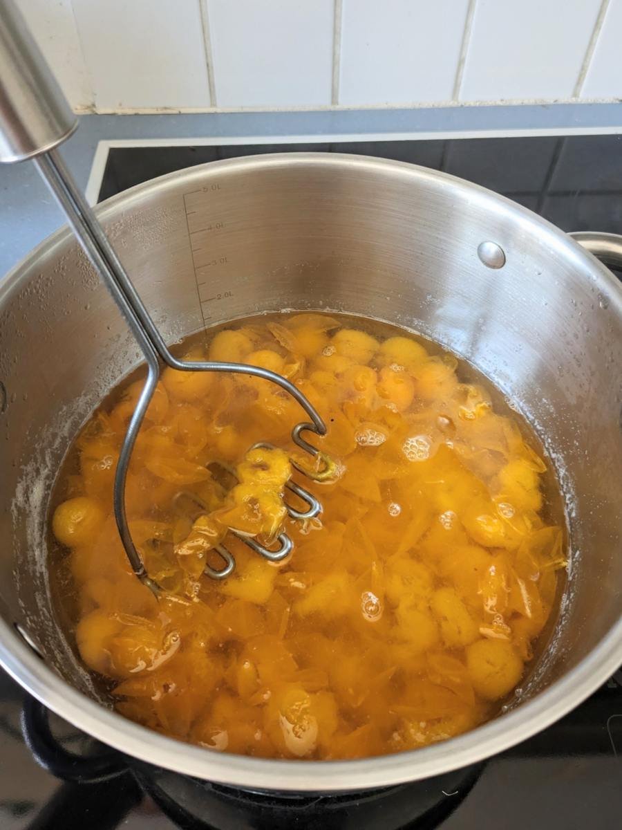 Softened Mirabelle plums being mashed in a saucepan before straining for plum cordial.
