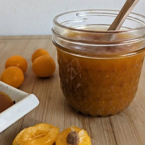 Jar of homemade slow cooker spiced plum butter with fresh Mirabelle plums.