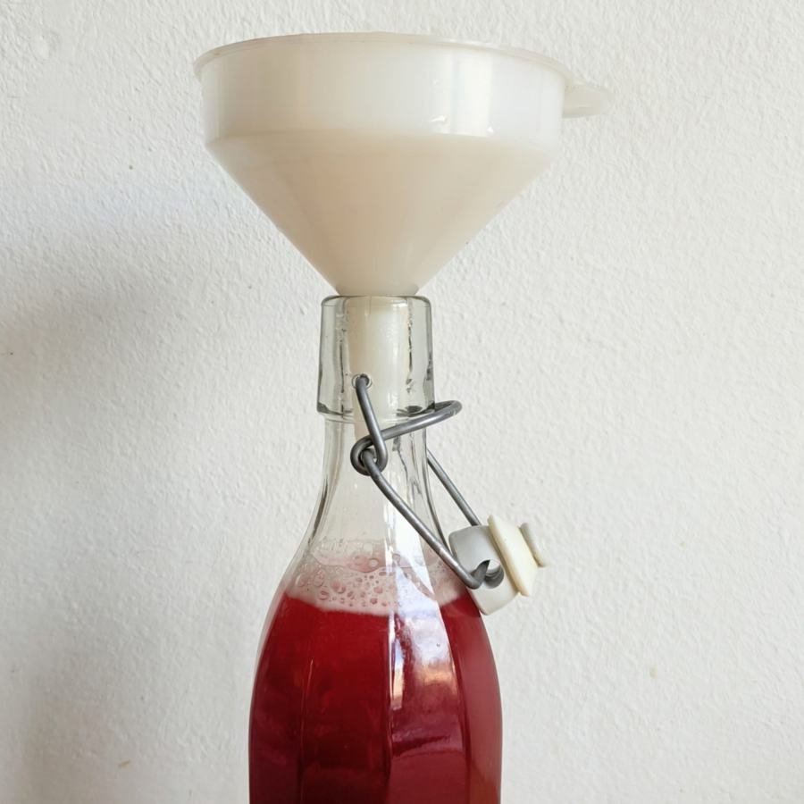 Lingonberry syrup being poured through a funnel into a clean glass bottle.