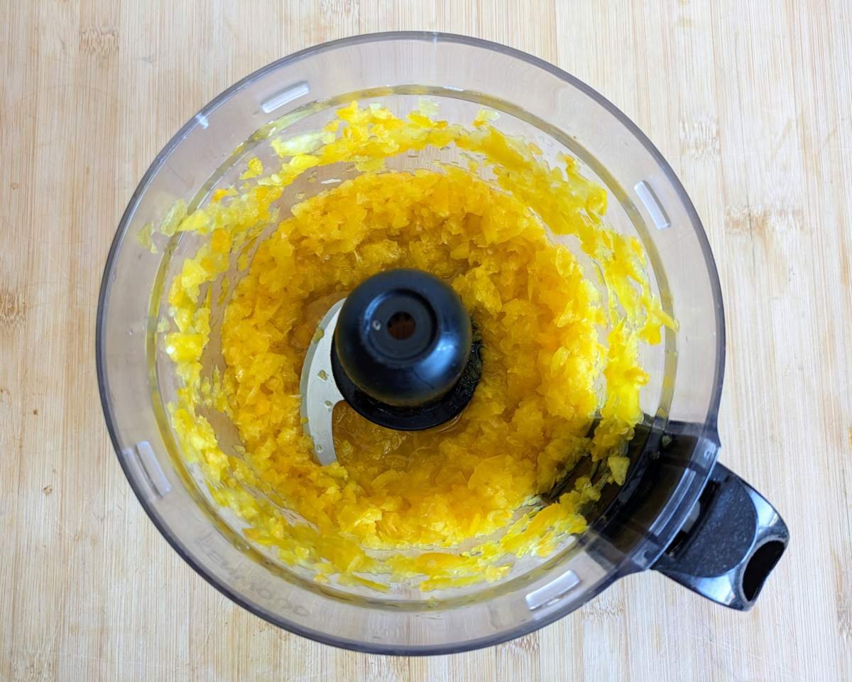 Alt text: Finely chopped yellow peppers and chillies in a food processor, with small pieces still visible.