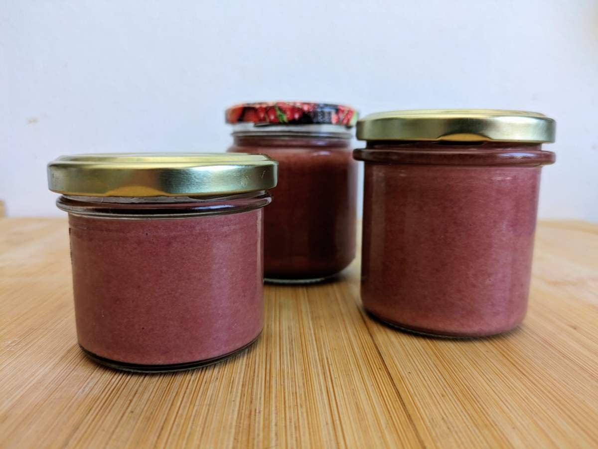 Three jars of Cornelian cherry curd on a wooden surface.