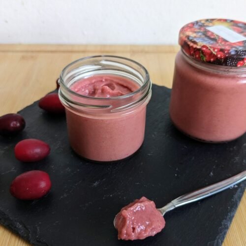 Cornelian cherry curd in glass jars with fresh Cornelian cherries and a spoonful of curd.