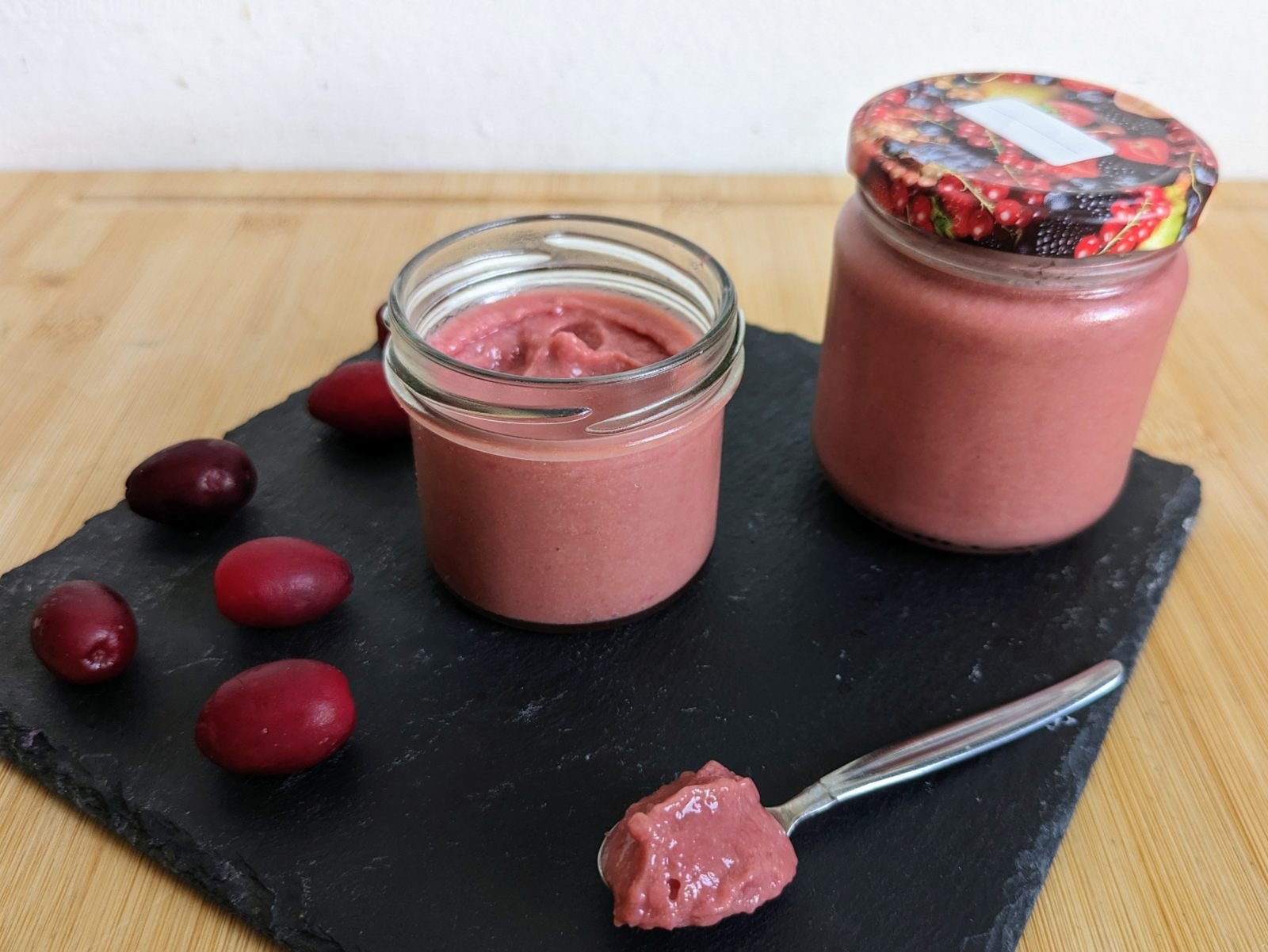 Cornelian cherry curd in glass jars with fresh Cornelian cherries and a spoonful of curd.
