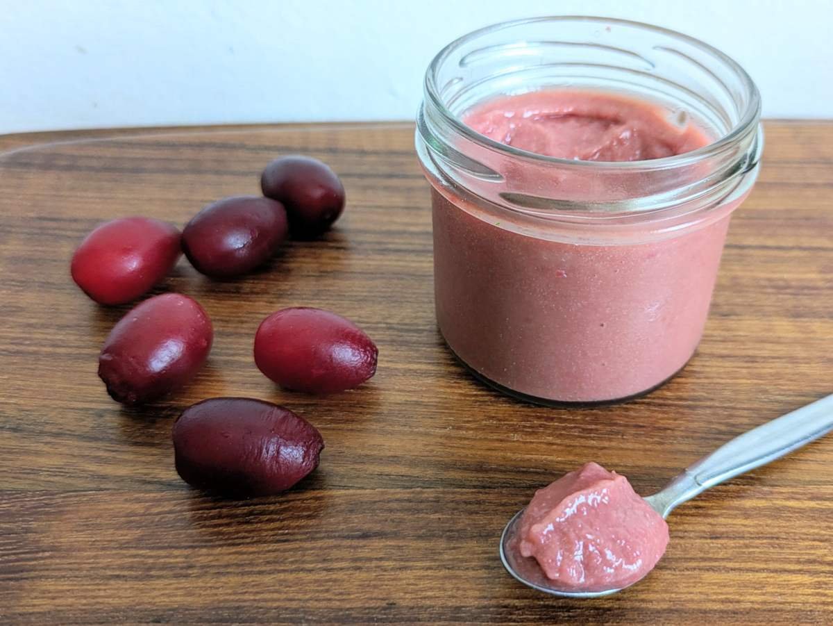 Cornelian cherry curd in a glass jar with fresh Cornelian cherries and a spoonful of curd.