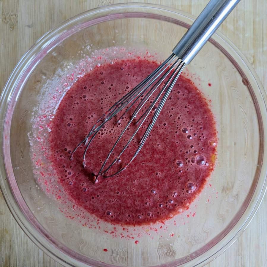 Cornelian cherry purée whisked with eggs in a glass bowl.