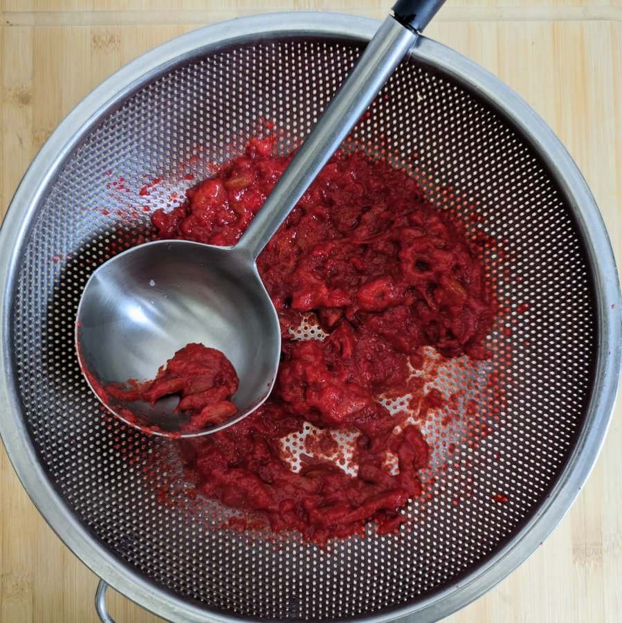 Cooked Cornelian cherries being pressed through a colander to remove the stones.