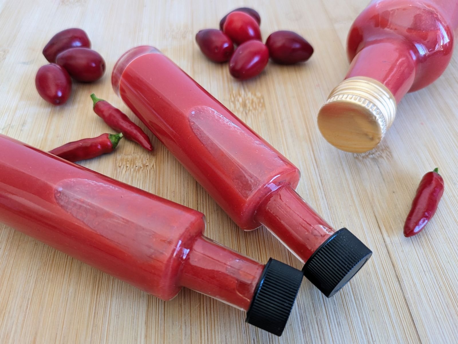 Cornelian cherry hot sauce in glass bottles with fresh Cornelian cherries and red chillies.