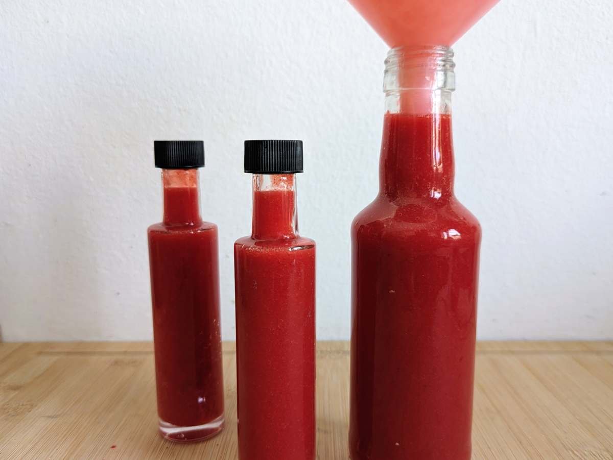 Cornelian cherry hot sauce being poured through a funnel into glass bottles.