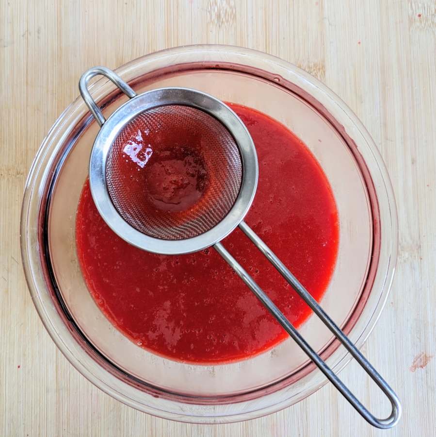 Cornelian cherry hot sauce being passed through a fine-mesh sieve for a smoother consistency.