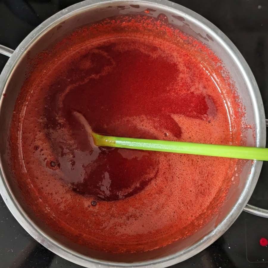 Cornelian cherry jam bubbling in a saucepan as it cooks and thickens.