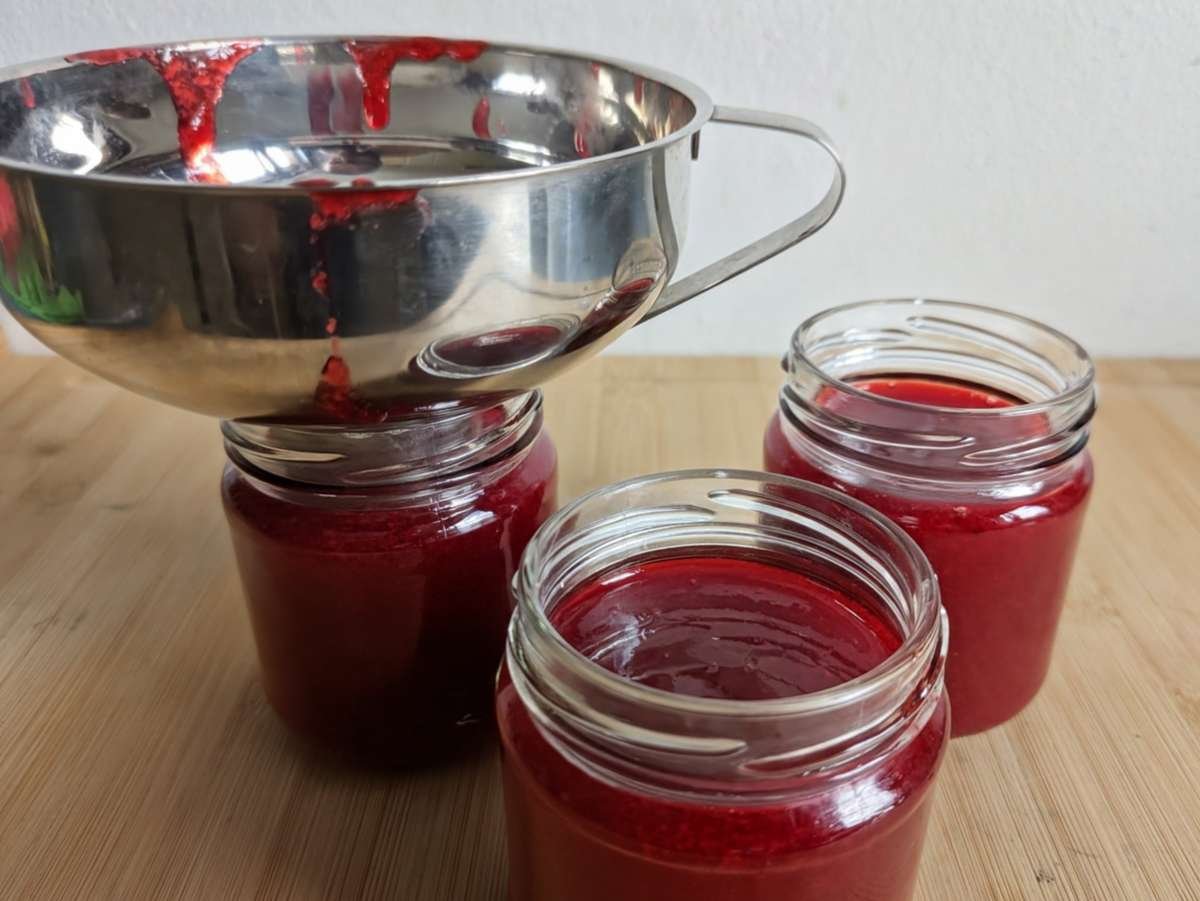 Hot Cornelian cherry jam being poured into clean glass jars.