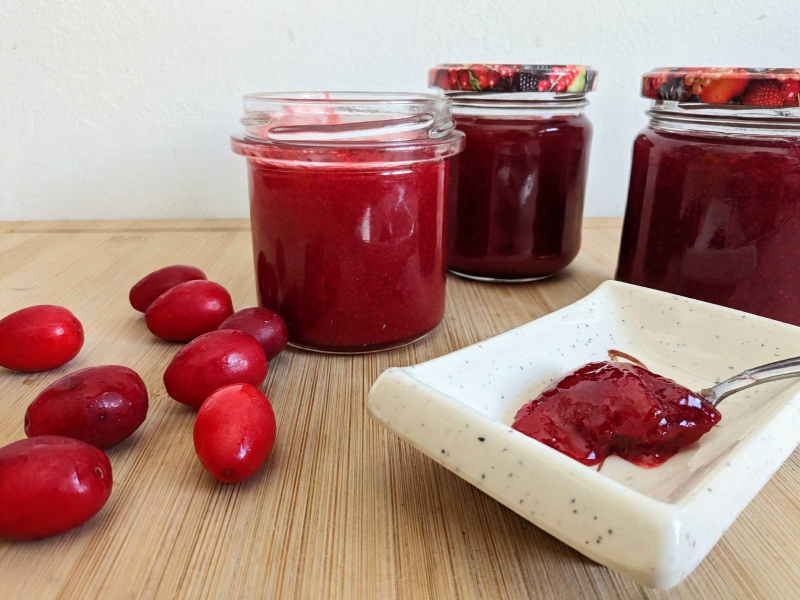 Cornelian cherry jam in glass jars with fresh cherries and a spoonful of jam.