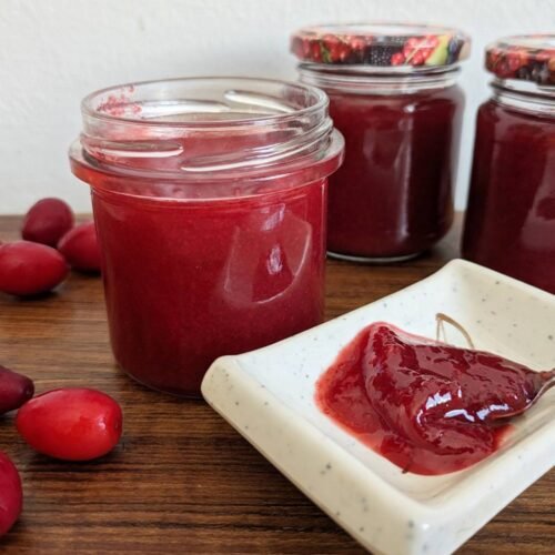 Homemade Cornelian cherry jam in glass jars with fresh cherries and a spoonful of jam.
