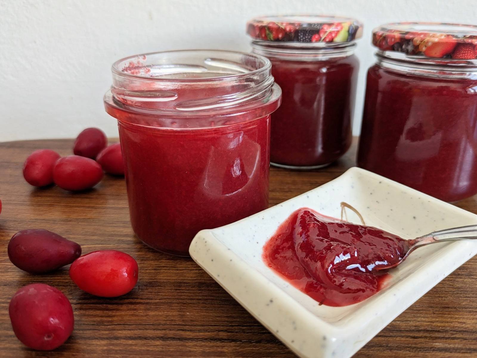 Homemade Cornelian cherry jam in glass jars with fresh cherries and a spoonful of jam.