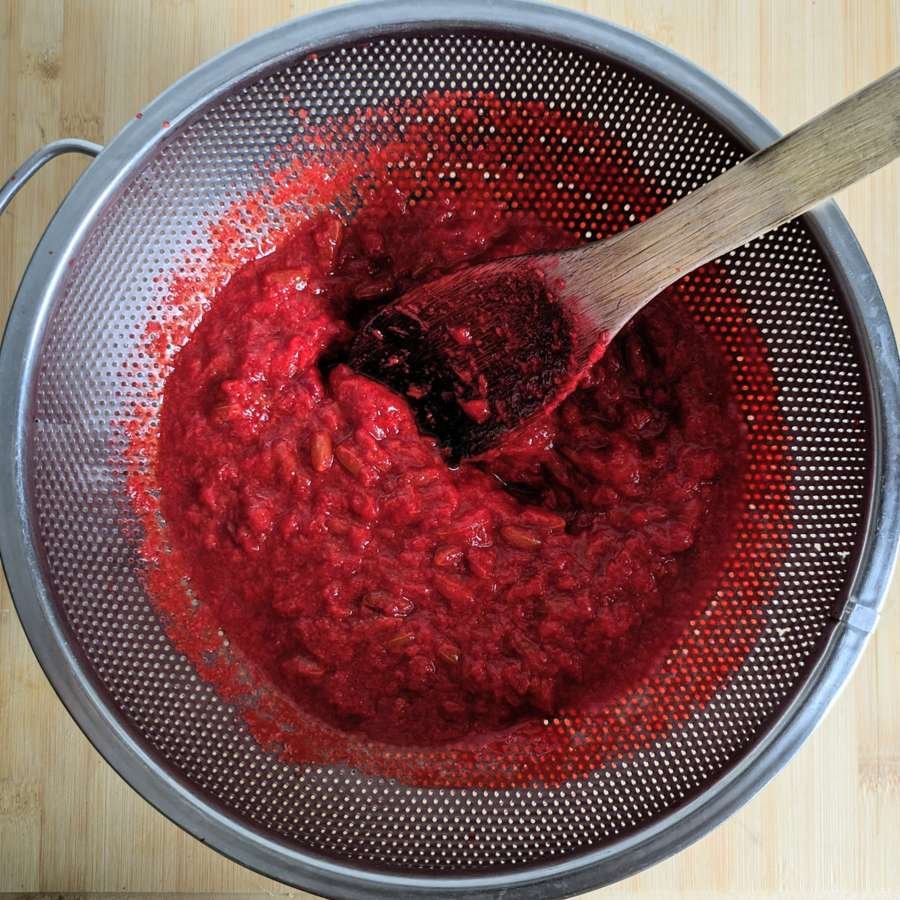 Cooked Cornelian cherries being pressed through a colander to remove the stones.