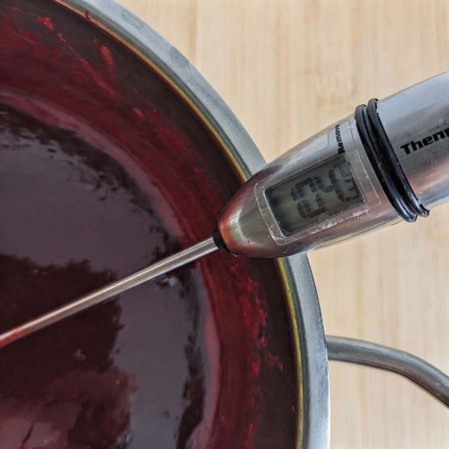 Cornelian cherry jam being checked with a thermometer for setting temperature.
