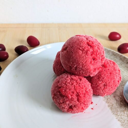 Three scoops of Cornelian cherry sorbet on a plate with fresh Cornelian cherries and a spoon.