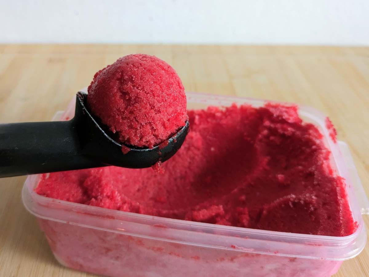 A scoop of Cornelian cherry sorbet being served from a container.