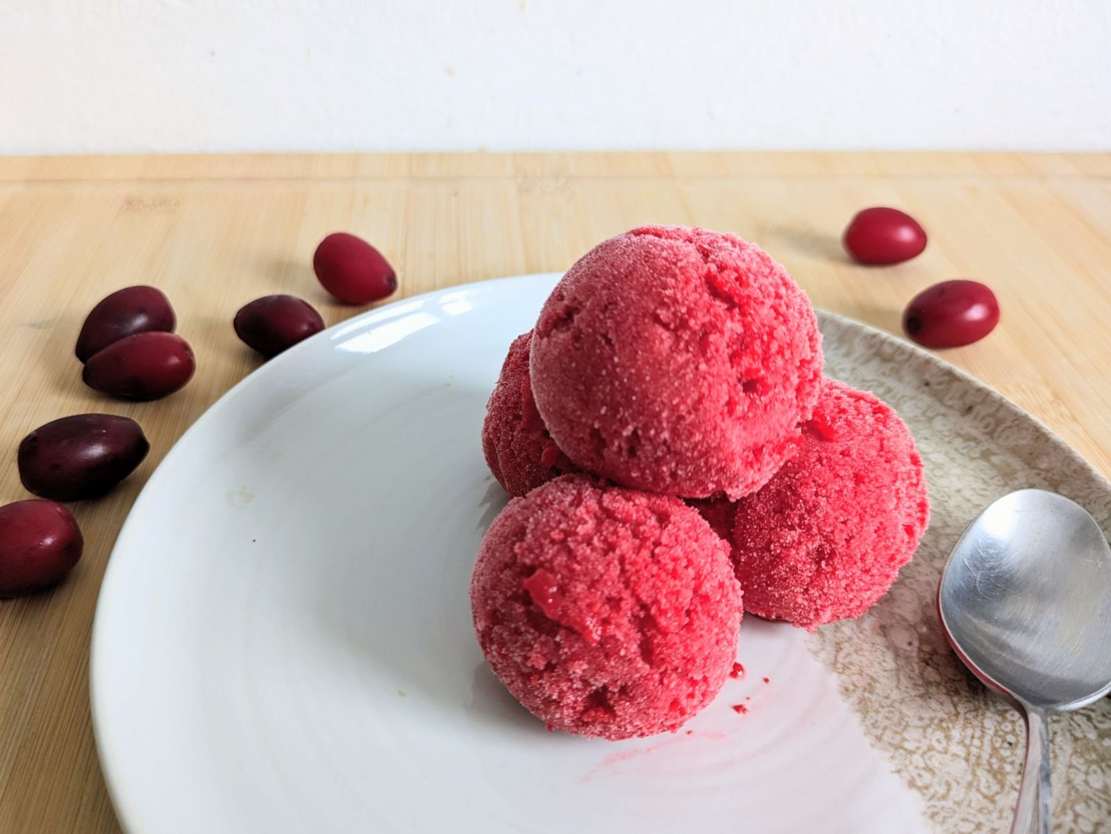 Three scoops of Cornelian cherry sorbet on a plate with fresh Cornelian cherries and a spoon.