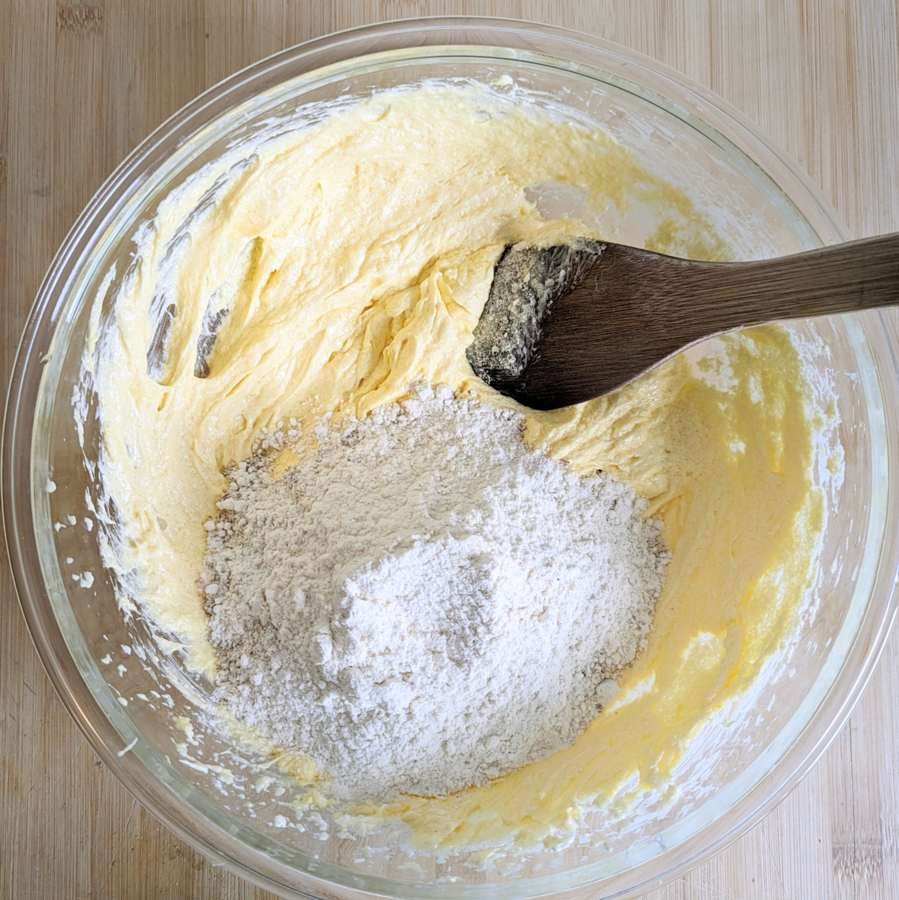 Folding flour and ground almonds into the cake batter with a wooden spoon.