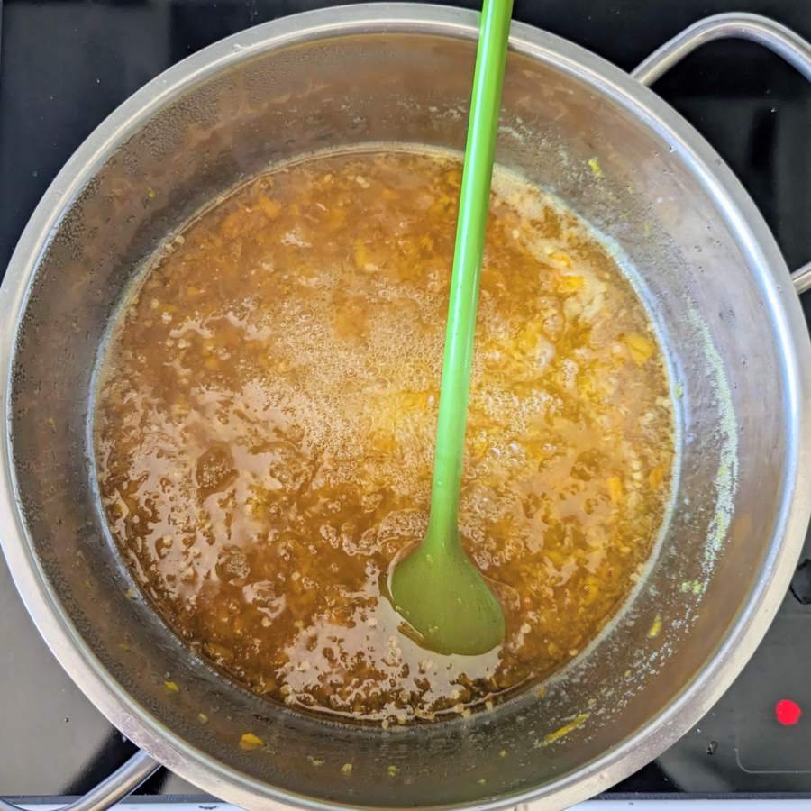 Golden chilli jam bubbling in a saucepan with a green spatula resting in it.